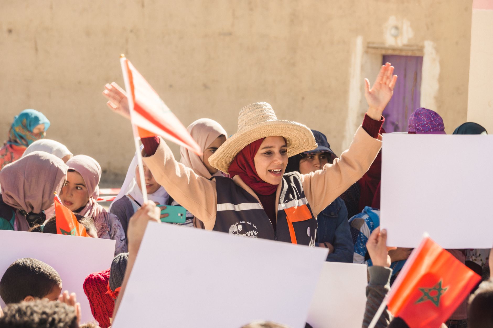 A group of women and children in Imilchil, Morocco demonstrating with Moroccan flags and signs.