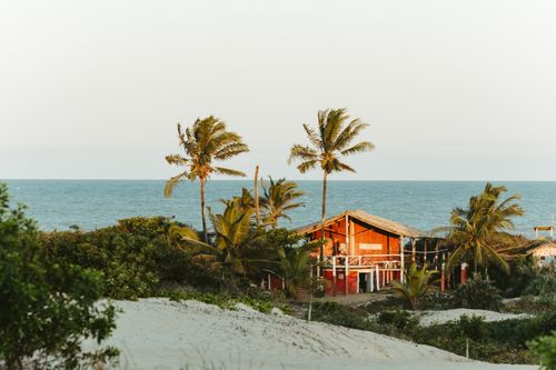 Free Scenic view of a rustic beach house in Itaúnas, surrounded by palms and sandy shores. Stock Photo