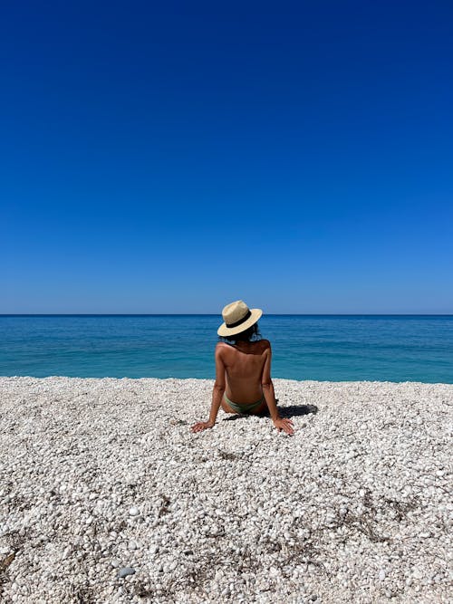 Back View of Topless Woman in Hat Sitting on Beach