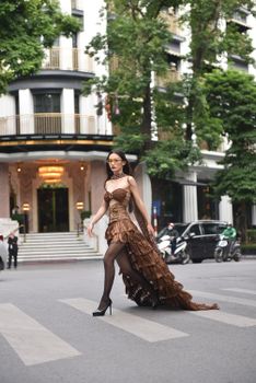 Fashionable woman in elegant dress crossing city street in urban setting, showcasing high fashion.