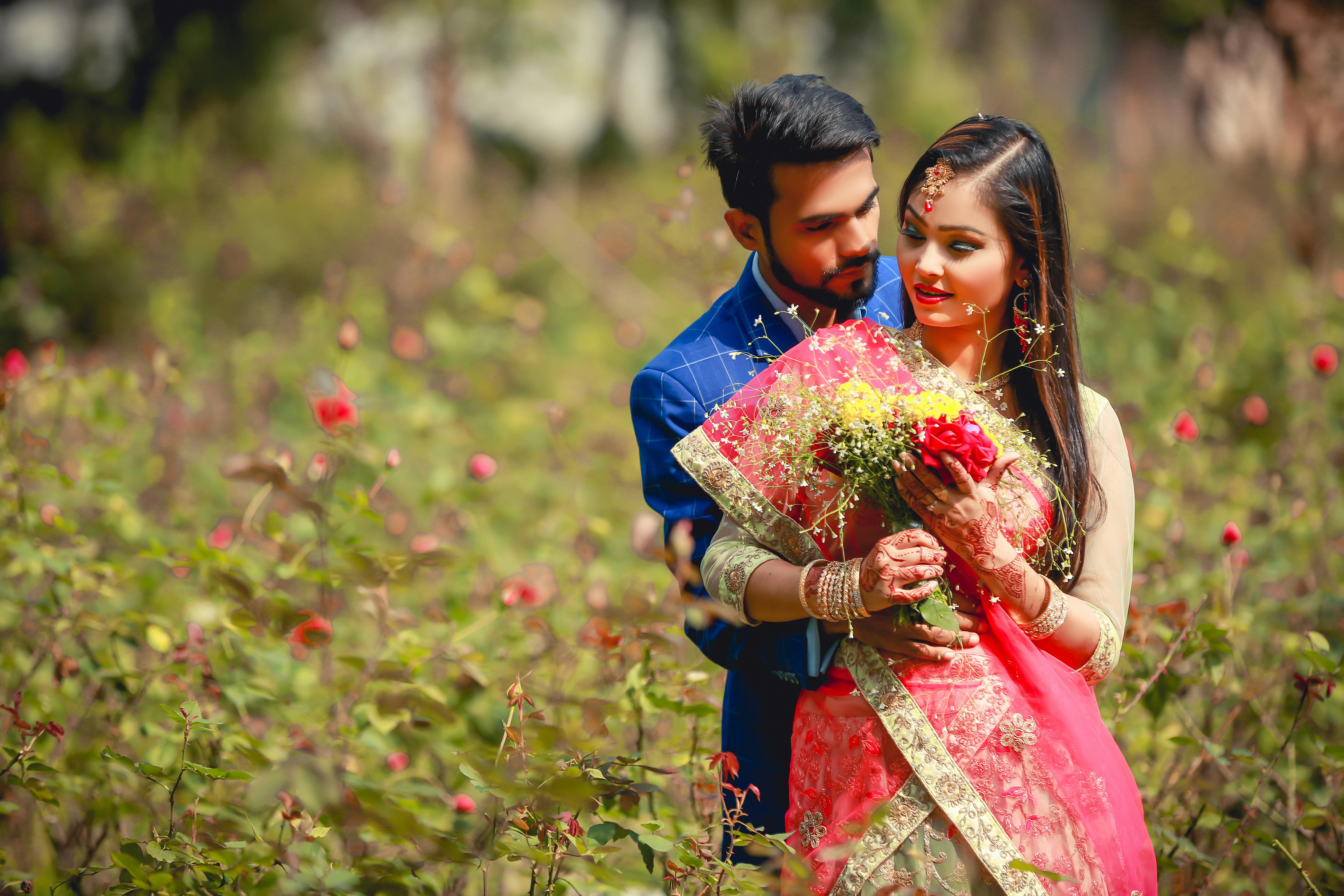 A newlywed couple in traditional attire embraces in a vibrant garden.