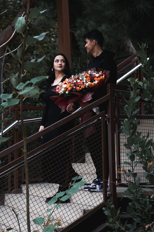 Smiling Couple with Bouquet of Flowers Standing on Stairs