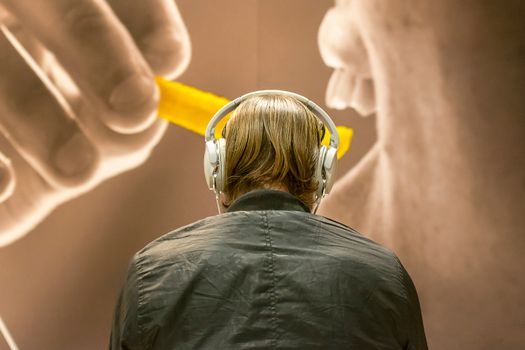 Rear view of a man with headphones engaged in an art exhibition with a large image projection.