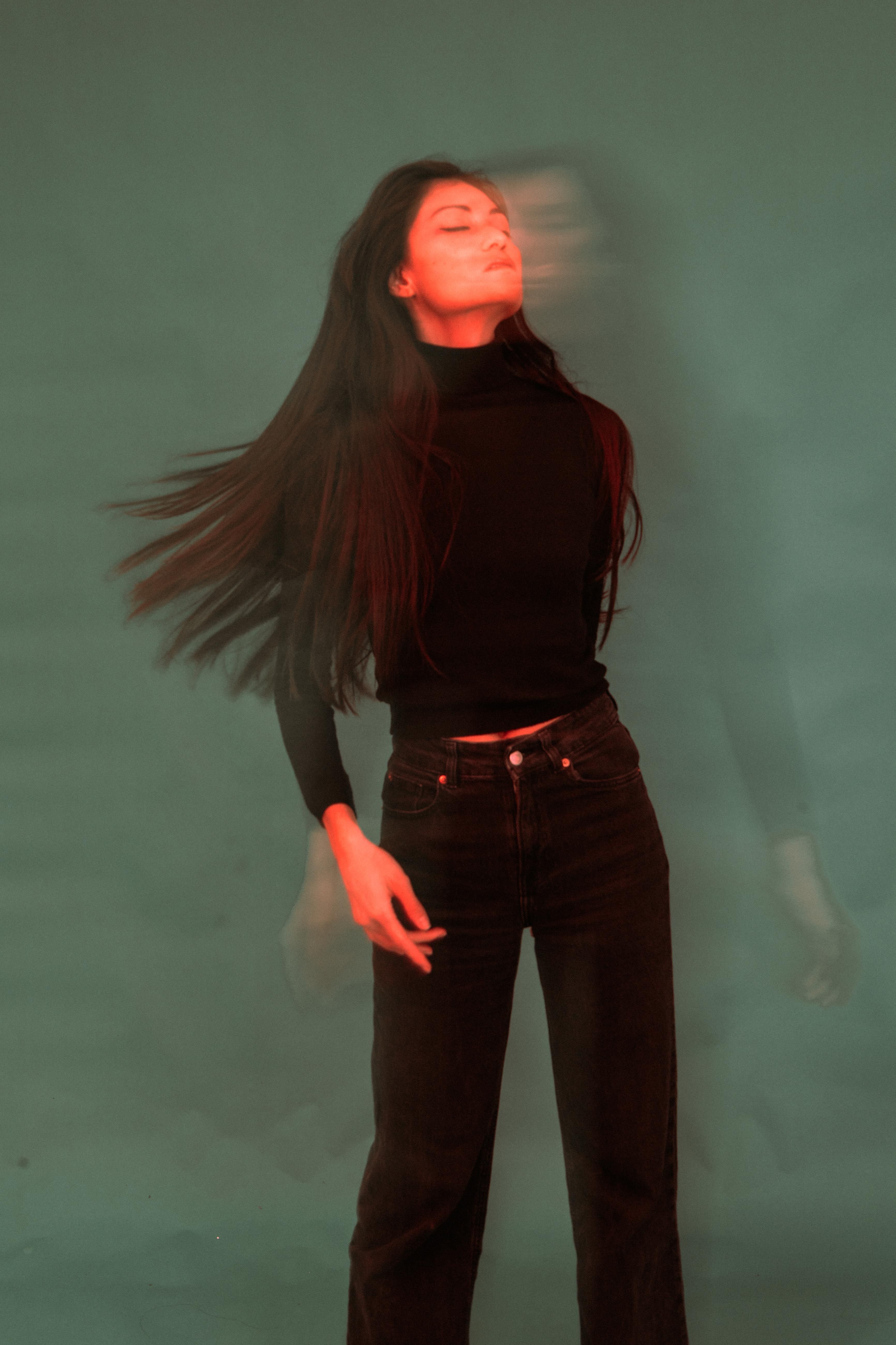 Artistic portrait of a woman with motion blur and long hair against a gray background.