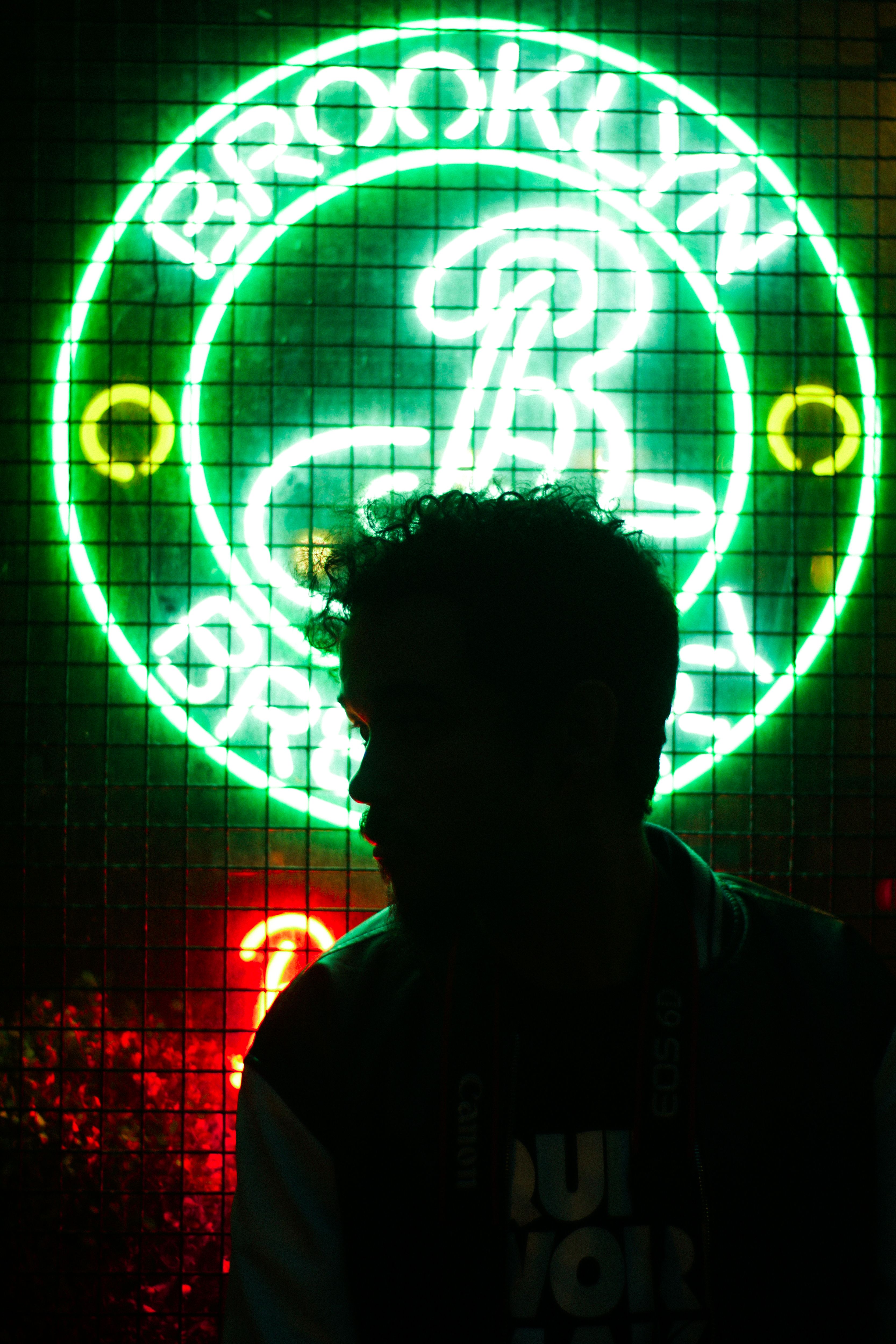 Silhouette of a man sitting in front of a bright neon Brooklyn Brewery sign at night.
