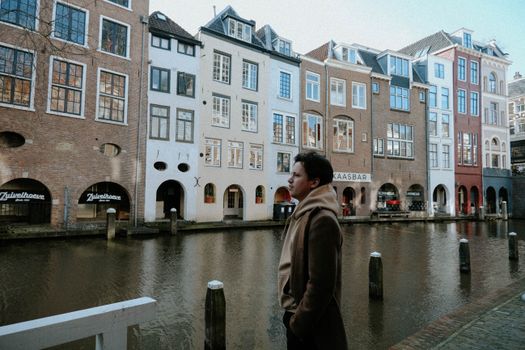 A man stands by a picturesque canal in Utrecht, Netherlands, showcasing historic architecture.