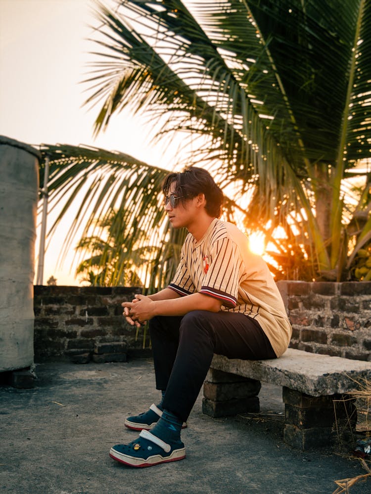 Man In Sunglasses Sitting On Stone Bench At Sunset