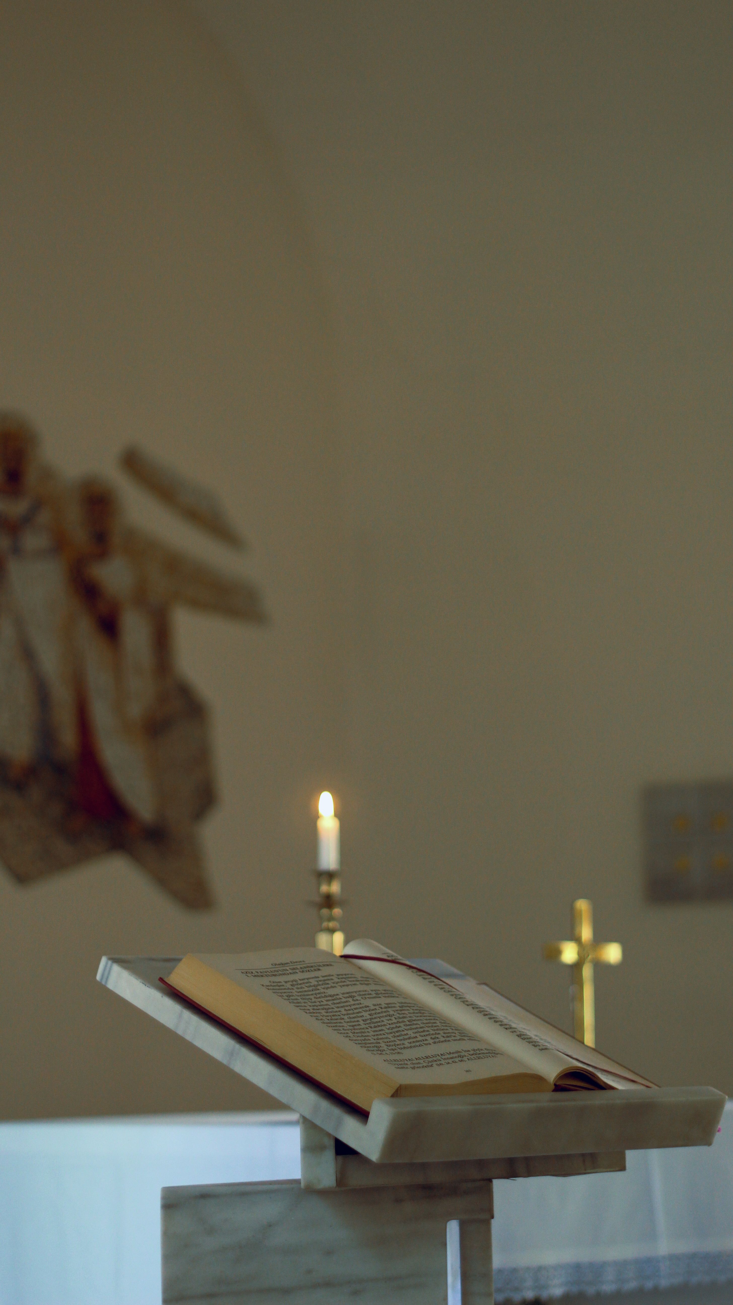 An open Bible on a stand with a lit candle in a church setting, conveying spirituality.
