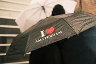 Close-up of umbrellas in a rainy Amsterdam day, featuring 'I love Amsterdam' slogan.