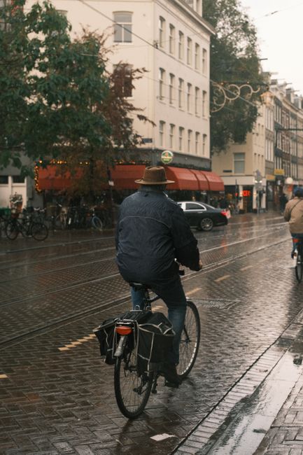 Cyclist rides on wet Amsterdam street, capturing urban rain atmosphere.