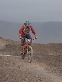 Man mountain biking on a challenging trail amidst desolate landscape, showcasing adventure and endurance.