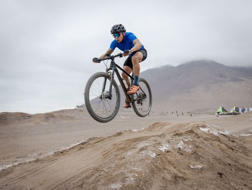 Free Male cyclist performs a jump on a mountain bike in a desert landscape, showcasing outdoor adventure. Stock Photo