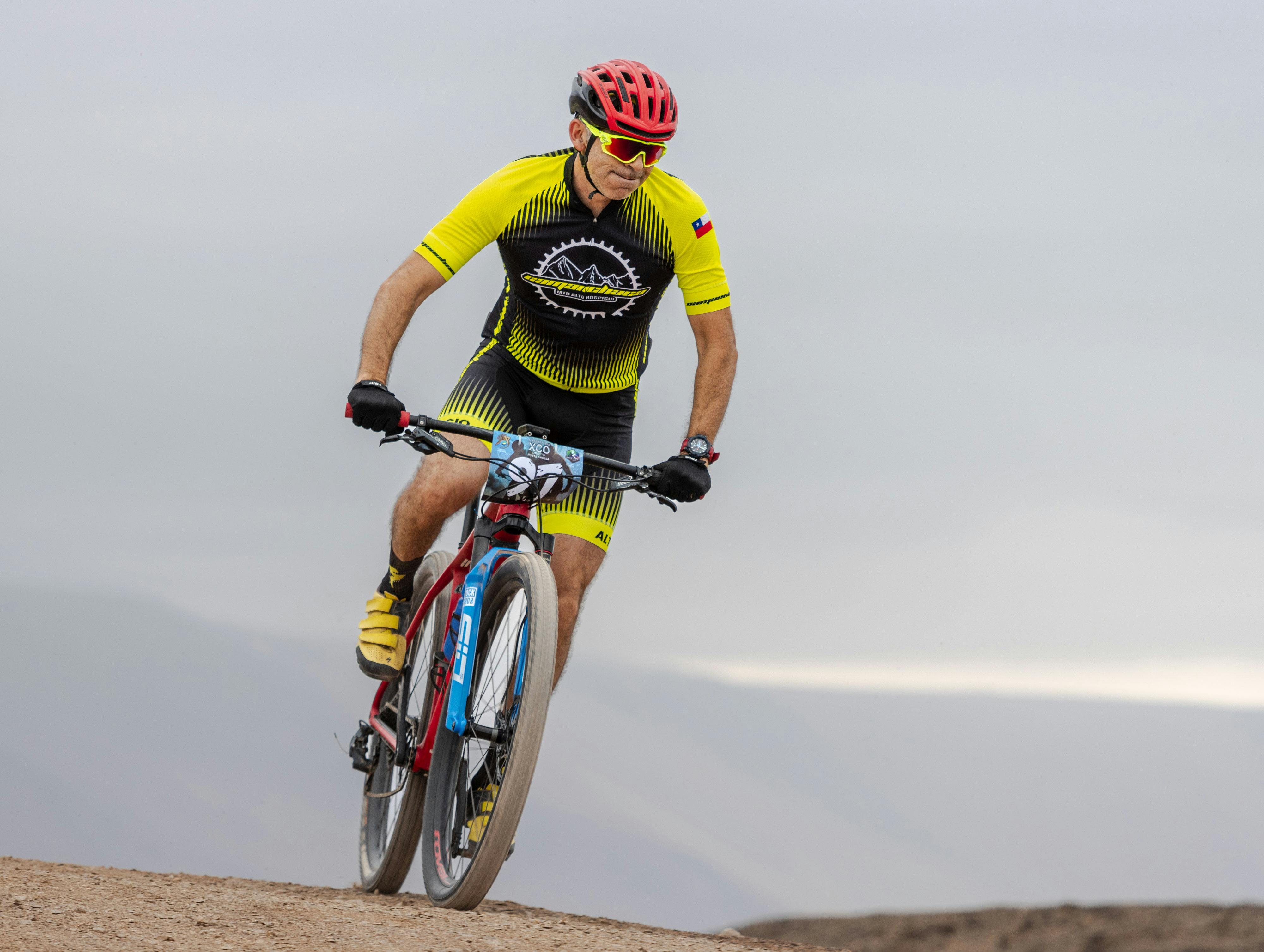 A cyclist wearing a red helmet and yellow outfit competes in a mountain bike race on a rugged trail.