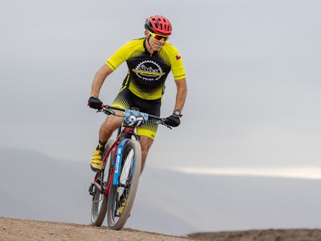 A cyclist wearing a red helmet and yellow outfit competes in a mountain bike race on a rugged trail.
