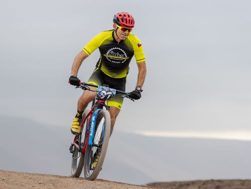 Free A cyclist wearing a red helmet and yellow outfit competes in a mountain bike race on a rugged trail. Stock Photo