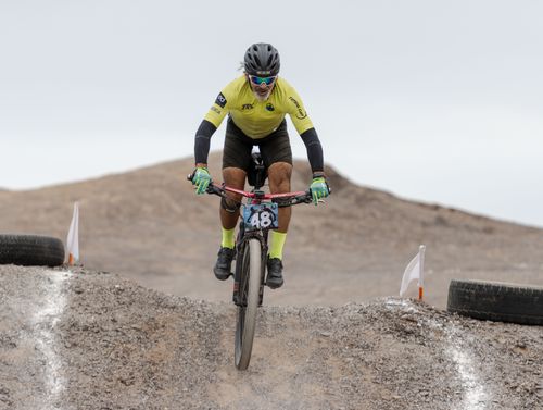 Free A cyclist in yellow gear performs a dirt jump in a desert setting. Stock Photo