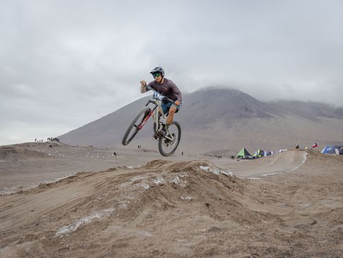 Free A mountain biker performs a jump on a dirt track set in a desert landscape under cloudy skies. Stock Photo