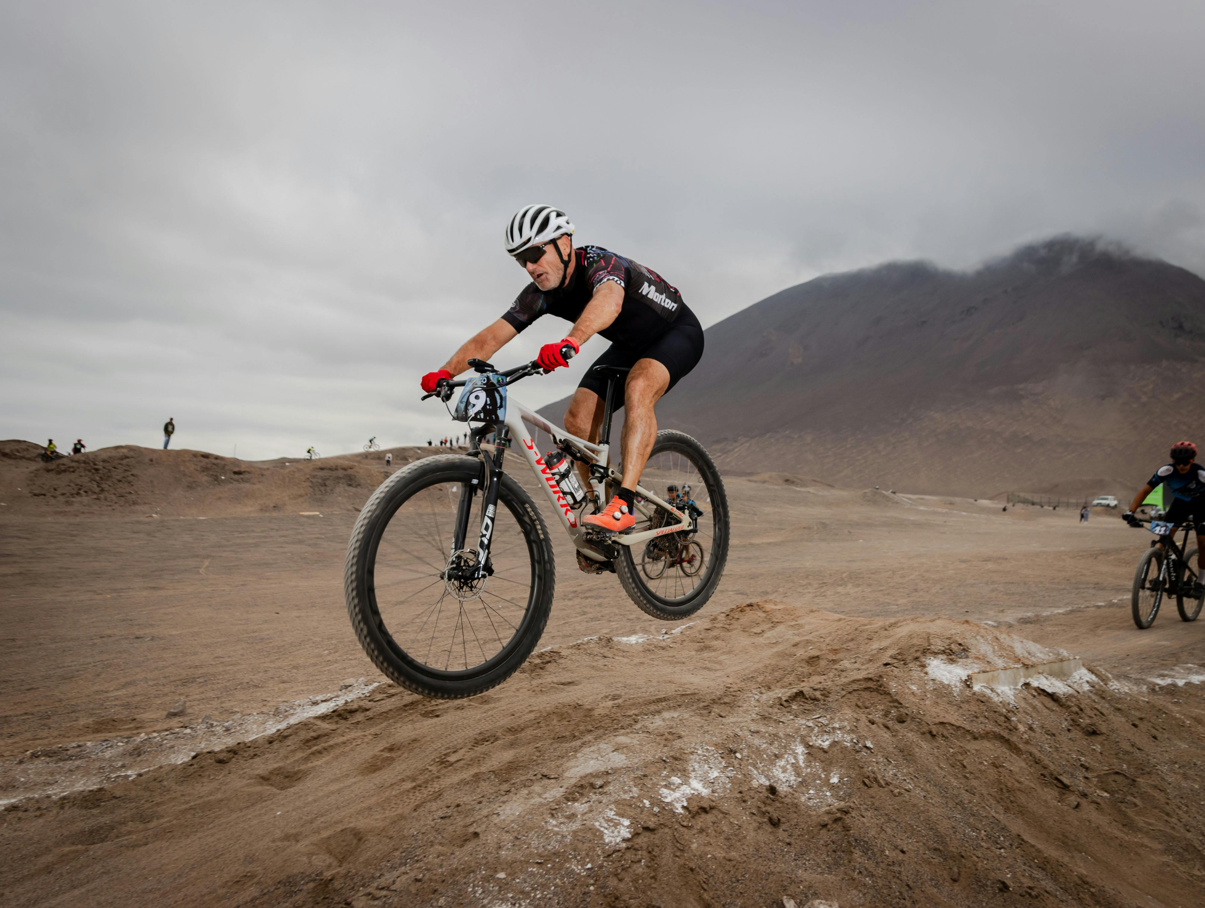 Athlete jumps over a dirt mound in an intense desert mountain biking race. Adventure and speed are captured.