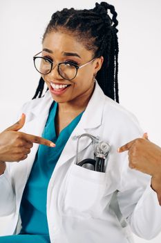 Cheerful female doctor in white coat pointing at stethoscope, embodying modern healthcare professionalism.