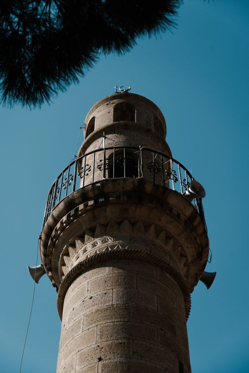 Free Low angle view of a historic stone minaret with intricate carvings under a blue sky. Stock Photo
