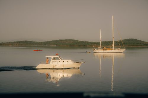 Free Peaceful lake scene with motorboat and sailboat reflections against a backdrop of lush hills. Stock Photo