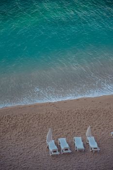 A peaceful beach with white loungers facing turquoise waves, inviting relaxation.