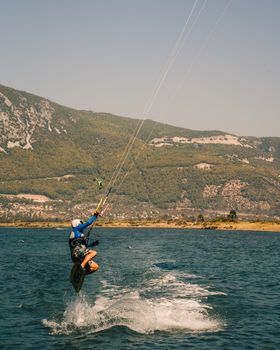 A dynamic kiteboarder jumps midair over the ocean with scenic mountain backdrop on a sunny day.