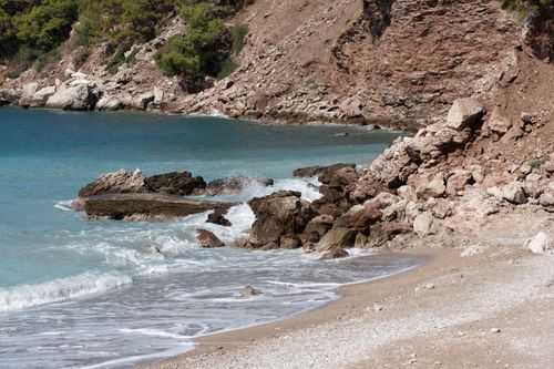 Free Tranquil beach scene with rocky shoreline and turquoise waters under clear skies. Stock Photo