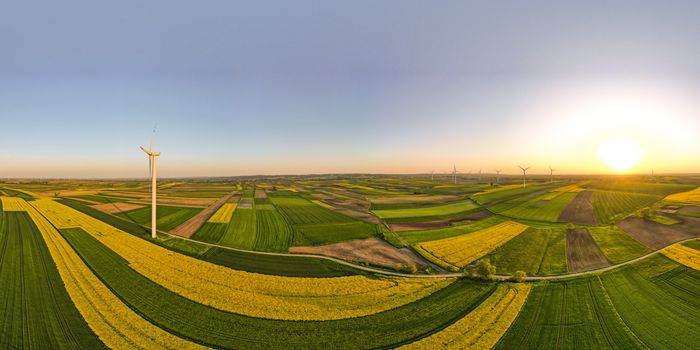 Aerial view of wind turbines amidst colorful farmland in Kosina, Poland during sunset.