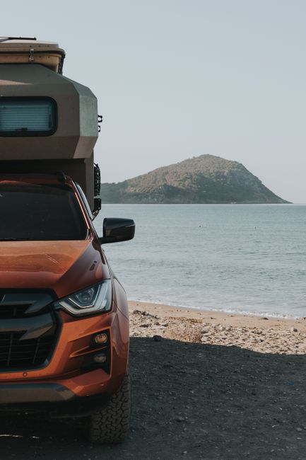 A camper van parked by a tranquil beach with a mountain view, ideal for summer travel.