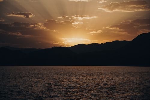 Free Serene sunset over mountains with dramatic sky and ocean view, perfect for tranquility themes. Stock Photo