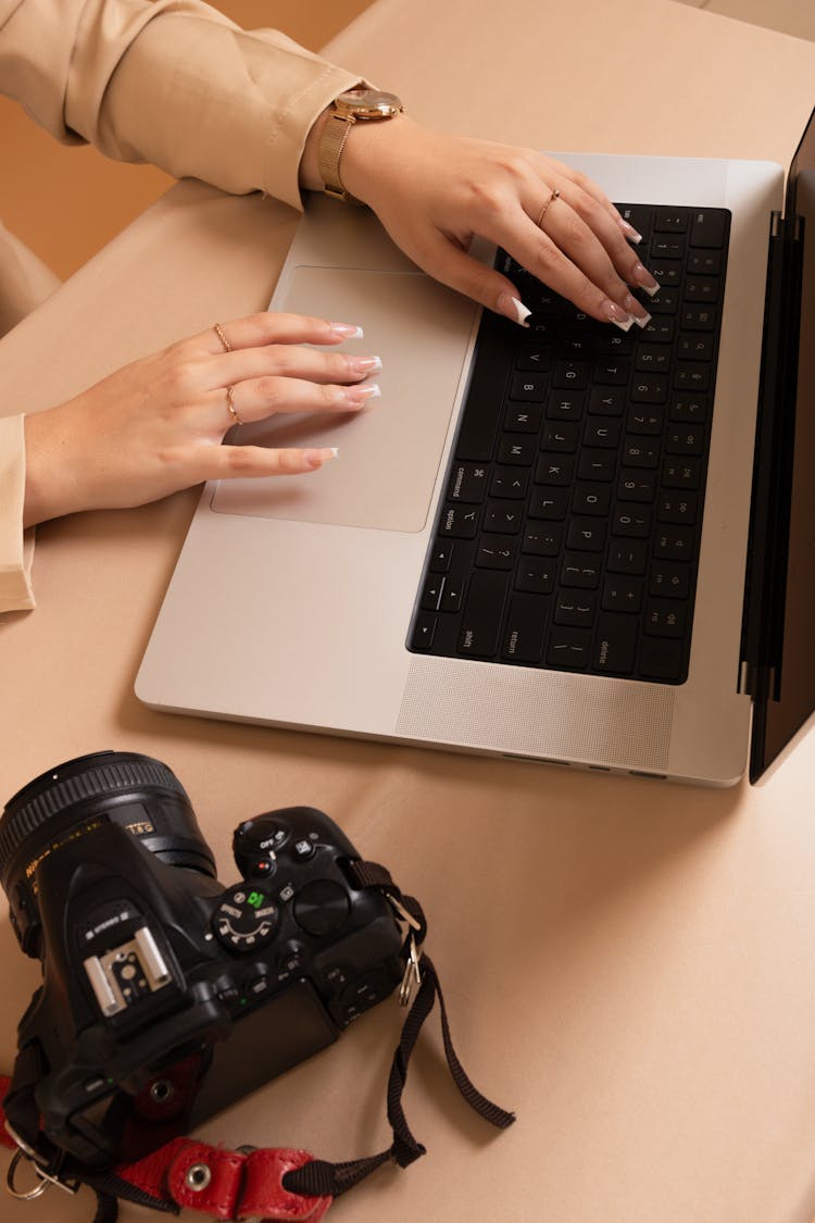 Woman Working On A Laptop With A Camera Lying Next To Her 