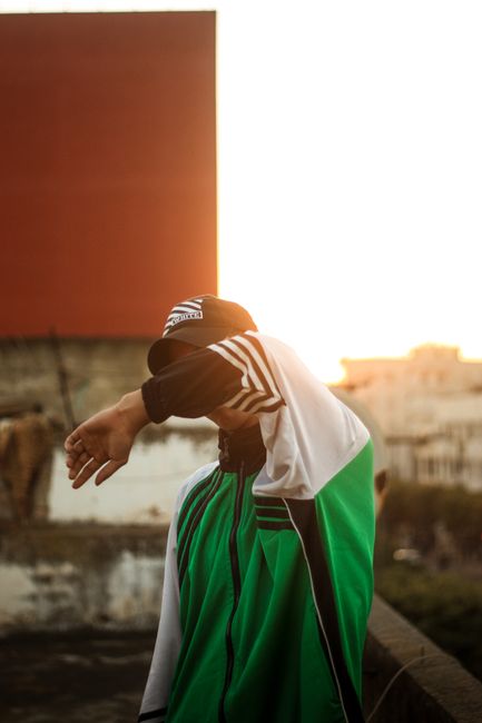 Stylish man in green jacket and cap outdoors during sunset, showcasing urban fashion vibes.
