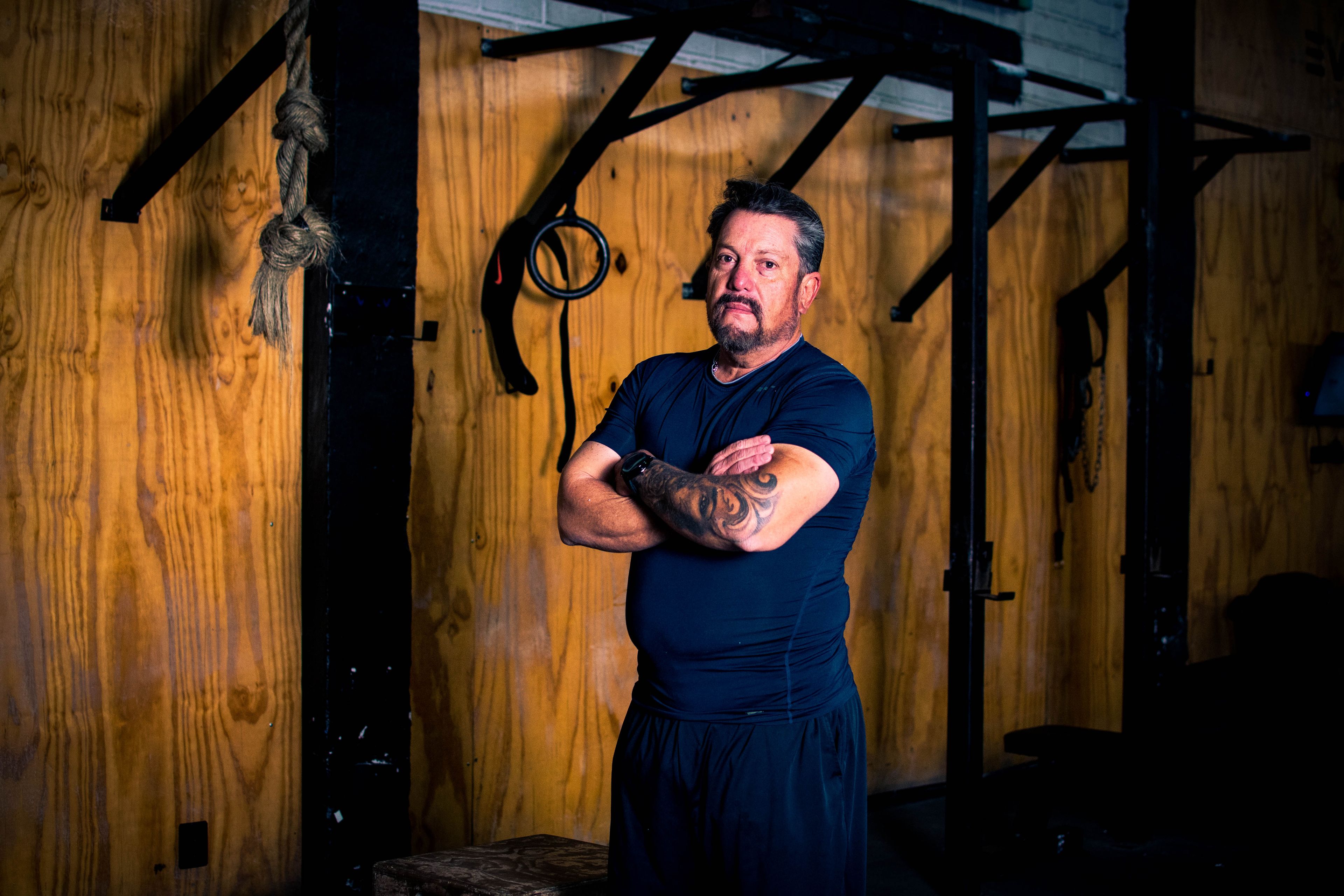 Mature man with tattoos stands confidently in a gym, showcasing sportswear and fitness.