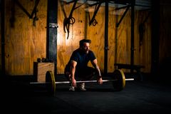 A man prepares to lift a barbell in a dimly lit gym environment, focusing on strength training.
