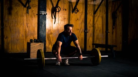 A man prepares to lift a barbell in a dimly lit gym environment, focusing on strength training.