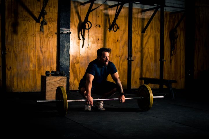 Lifter setting up under a loaded barbell in a dimly lit gym — photo by Hugazo Boss on Pexels
