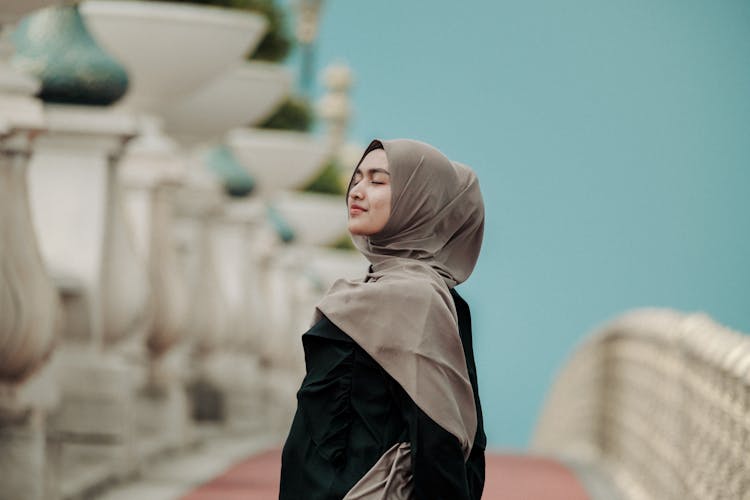 Young Woman In A Hijab Standing Outside With Eyes Closed And Smiling 