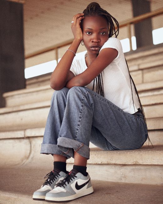 A young woman in casual streetwear and sneakers sits thoughtfully on concrete steps outdoors.
