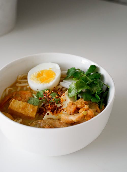 White Bowl of Coconut Noodle Soup with Egg on a Table