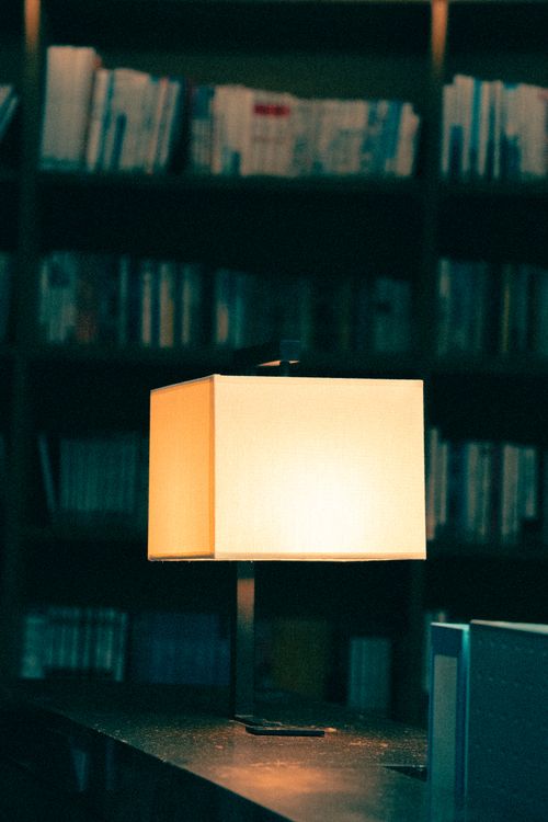 Free Warmly lit library scene featuring a modern lamp and shelves filled with books. Stock Photo