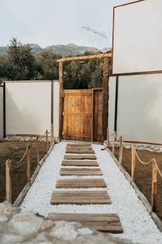 Explore this rustic wooden gate and white pebble path in Ortaca, Muğla, Türkiye, set against a tranquil garden backdrop.