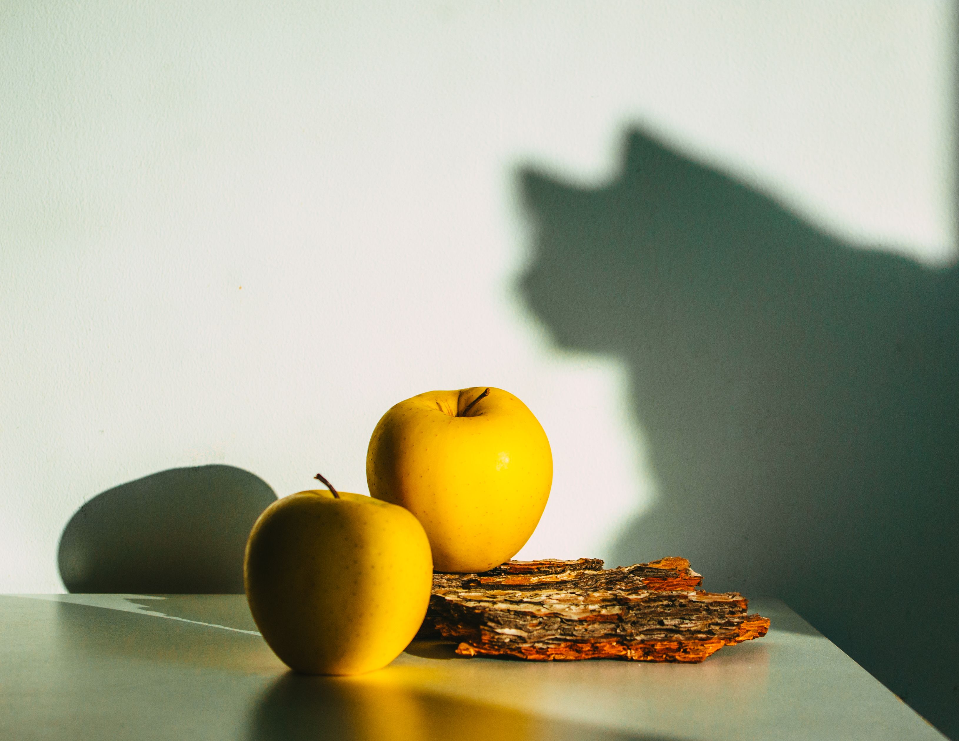 Yellow apples with bark casting a playful cat shadow in warm sunlight.