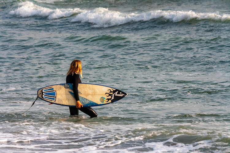 Surfer Walking In Ocean With Board Under Arm