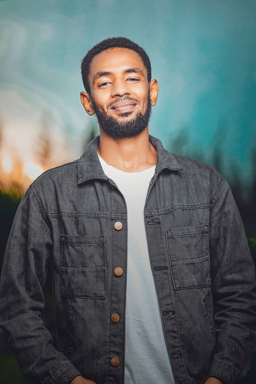 Free Smiling man in a denim jacket standing outdoors on a bright day. Stock Photo