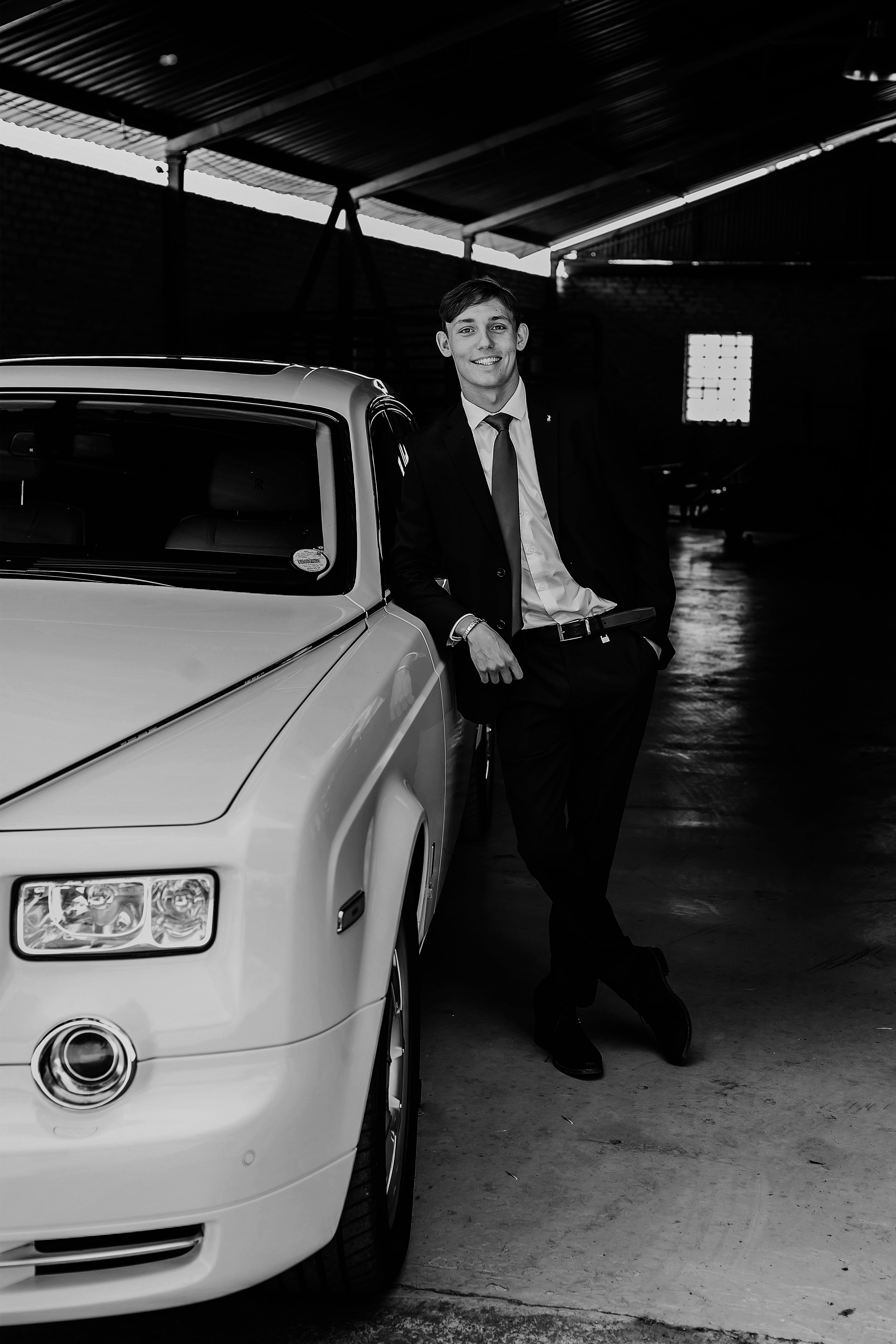 Black and white portrait of a man posing confidently by a luxury car in a garage.