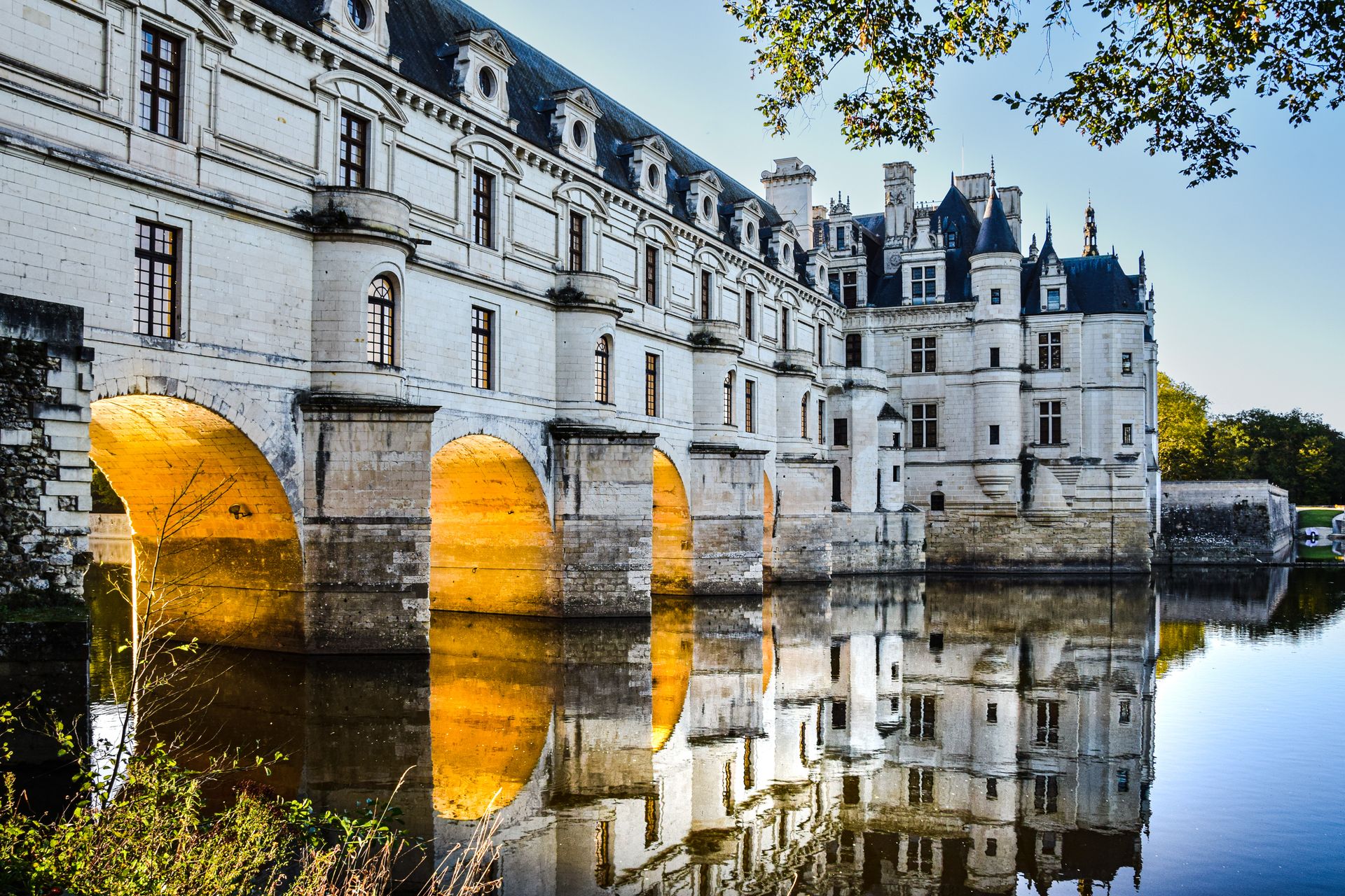 Historic Château de Chenonceau over a river with illuminated arches at dusk.