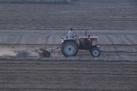A farmer operates a tractor for harrowing soil in a vast field, capturing early morning labor.