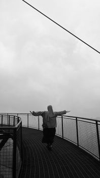 A woman stands with arms spread on an East Java observation deck, embracing the overcast sky.