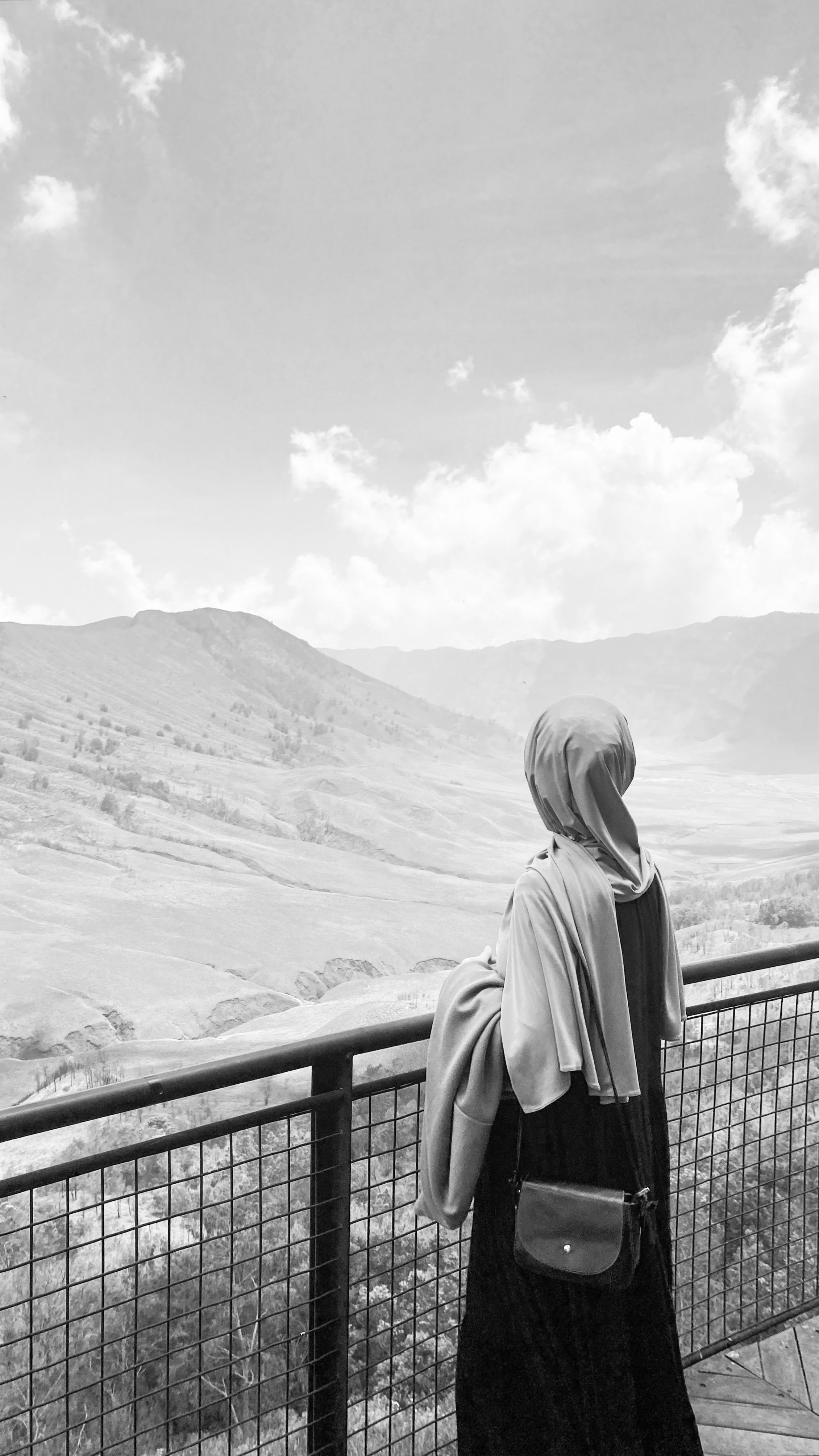 A woman in a headscarf gazes at the vast Indonesian landscape, captured in black and white.